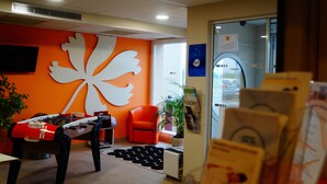 Una habitación con una mesa de futbolín, una silla naranja, un adorno blanco grande en la pared y una ventana con vistas al exterior.