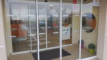 A hotel entrance with glass doors, a sign for a point of sale, and a small potted plant.