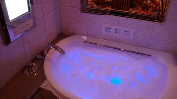 A modern bathroom with a large bathtub, a digital clock, and a mirror with a floral decoration.