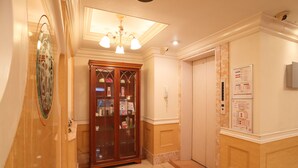 Un couloir avec une armoire en bois, un luminaire au plafond et un panneau fixé au mur.
