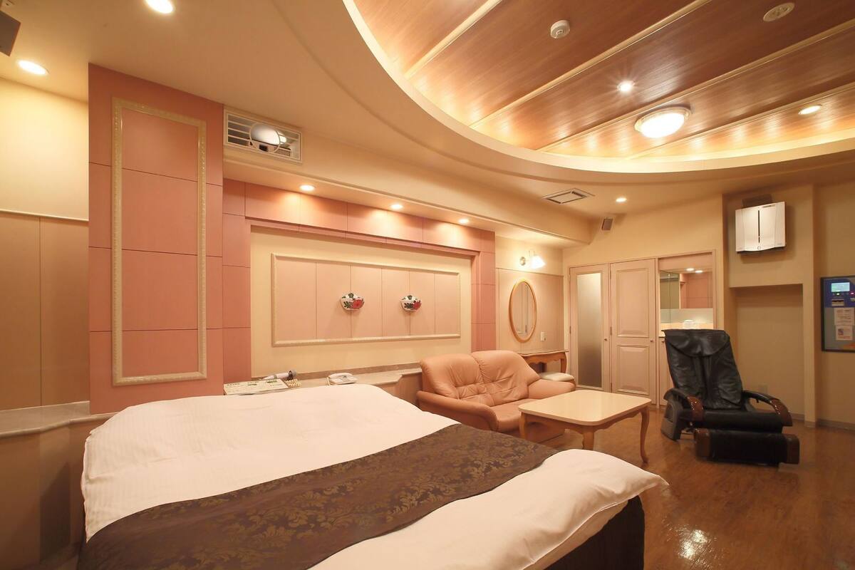 Une chambre d’hôtel dotée d’un grand lit, d’un coin salon avec un fauteuil, d’un bureau et d’un fauteuil massant.