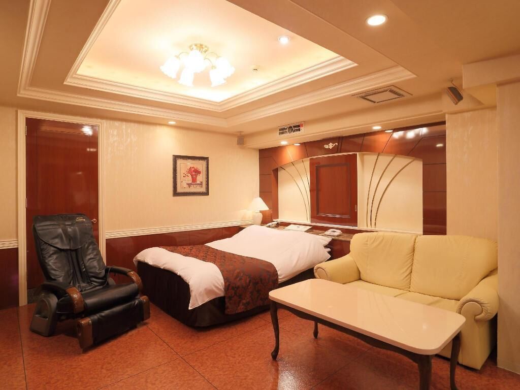Une chambre d’hôtel équipée d’un lit, d’un fauteuil massant, d’un canapé, d’une petite table et d’un luminaire au plafond.