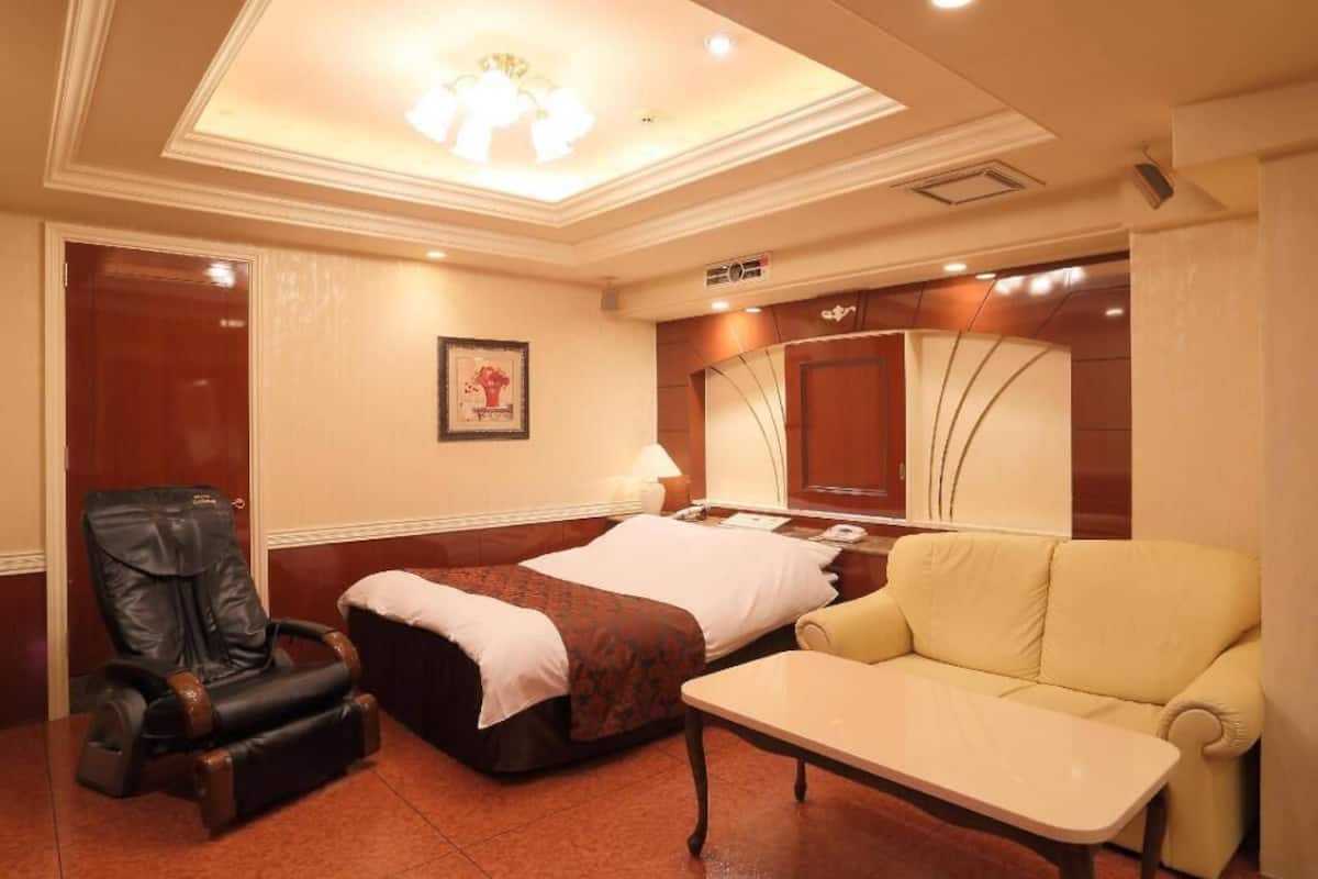 Une chambre d’hôtel équipée d’un lit, d’un fauteuil massant, d’un canapé, d’une petite table et d’un luminaire au plafond.