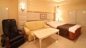 Une chambre d’hôtel comprenant un lit, un canapé, un fauteuil massant, une petite table et un luminaire au plafond.
