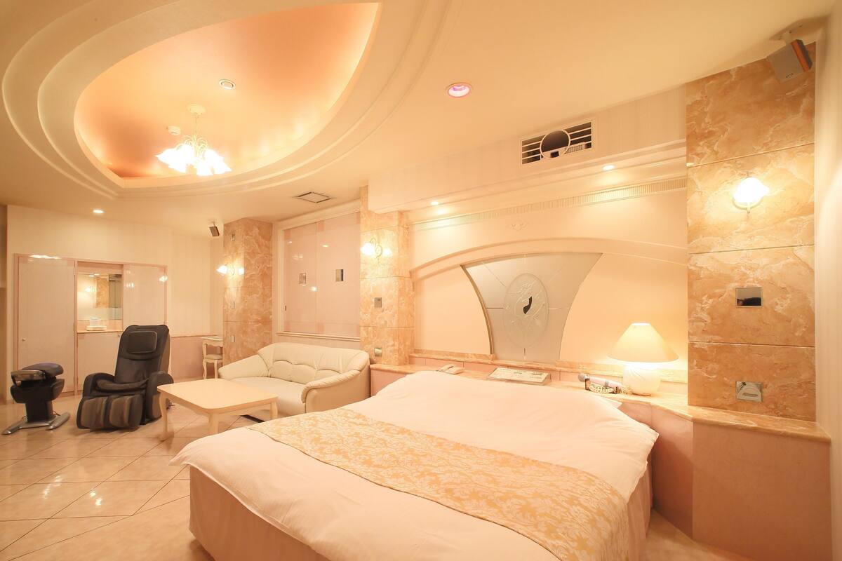 A spacious bedroom with a large bed, two armchairs, a desk, and a vanity with a mirror.