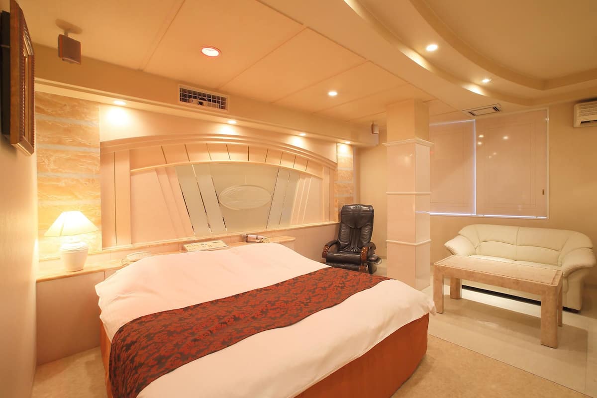 Une chambre à coucher avec un grand lit, un fauteuil de massage, un canapé et une fenêtre avec des stores.