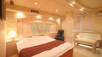 A bedroom with a large bed, a massage chair, a sofa, and a window with blinds.