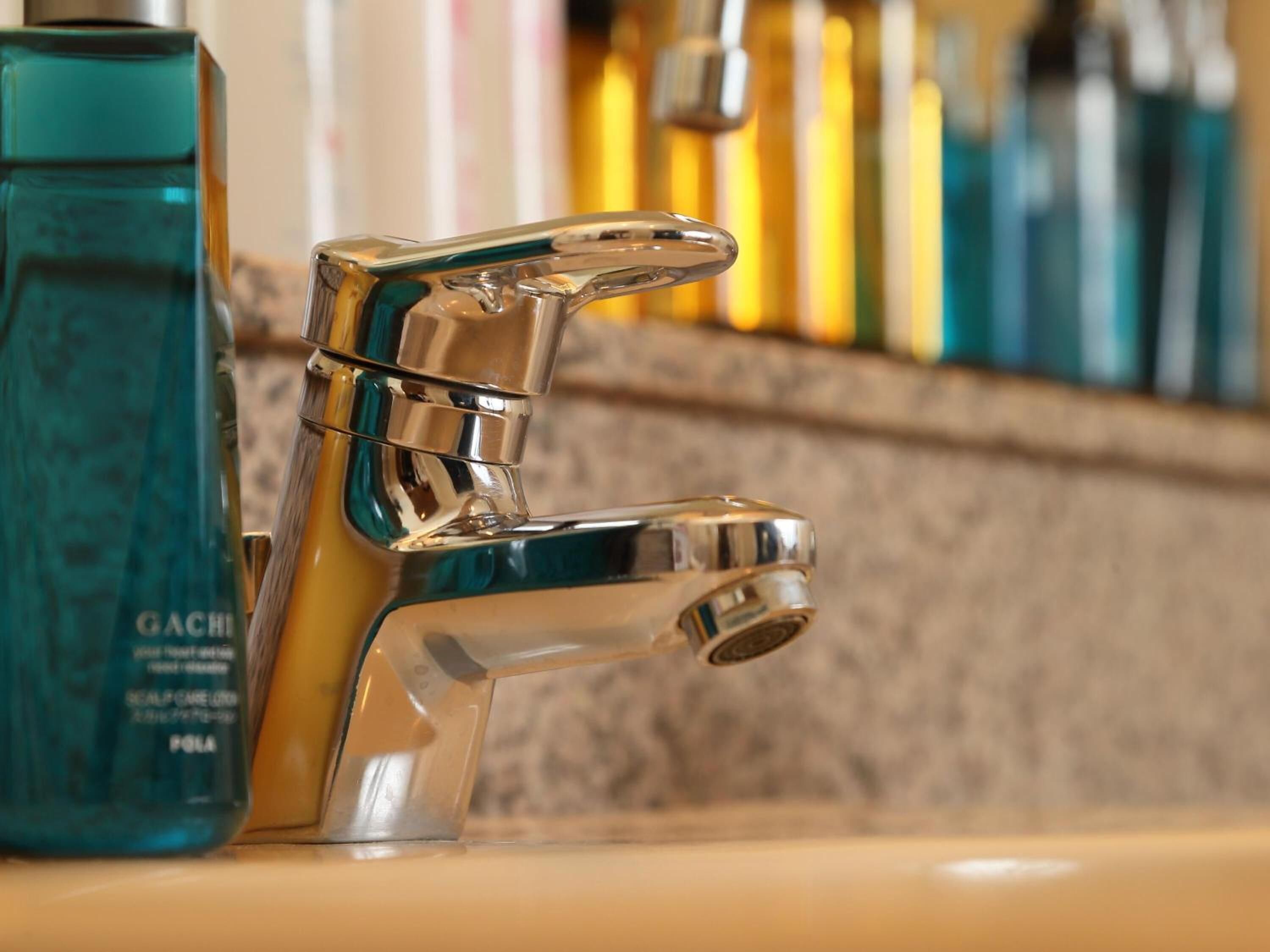 A chrome faucet with a modern design, positioned next to a teal bottle of GACHIN hair care product.