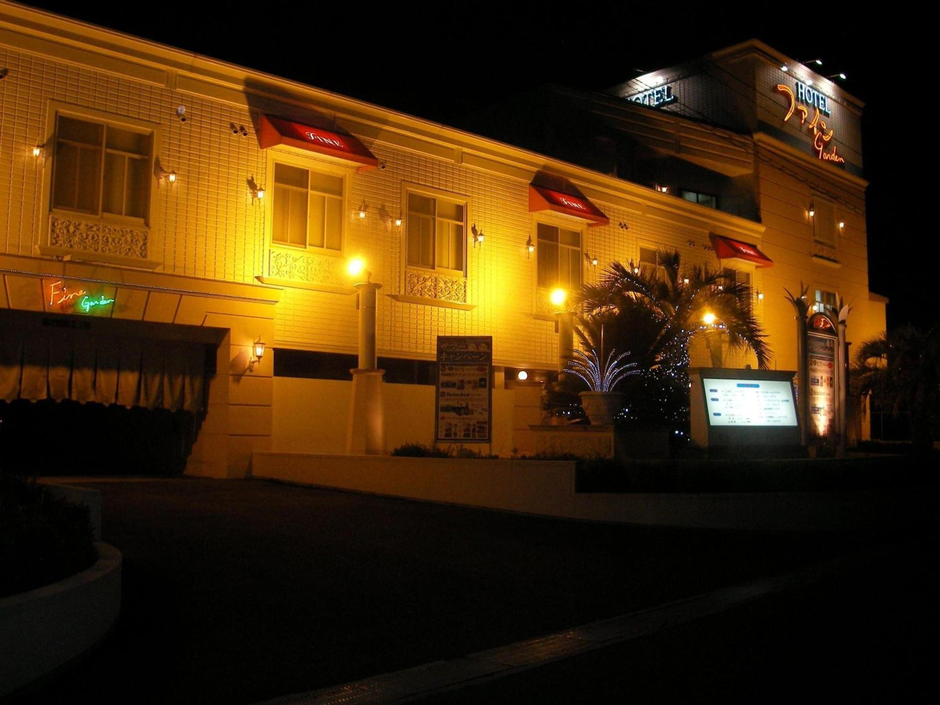 A hotel with a tiled facade, illuminated signage, and a palm tree in the foreground.