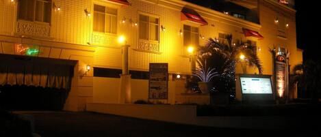 A hotel with a tiled facade, illuminated signage, and a palm tree in the foreground.