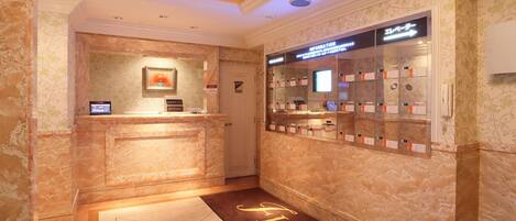 A hotel reception area with a marble counter, a digital information board, a reception desk, and a directory with room numbers.