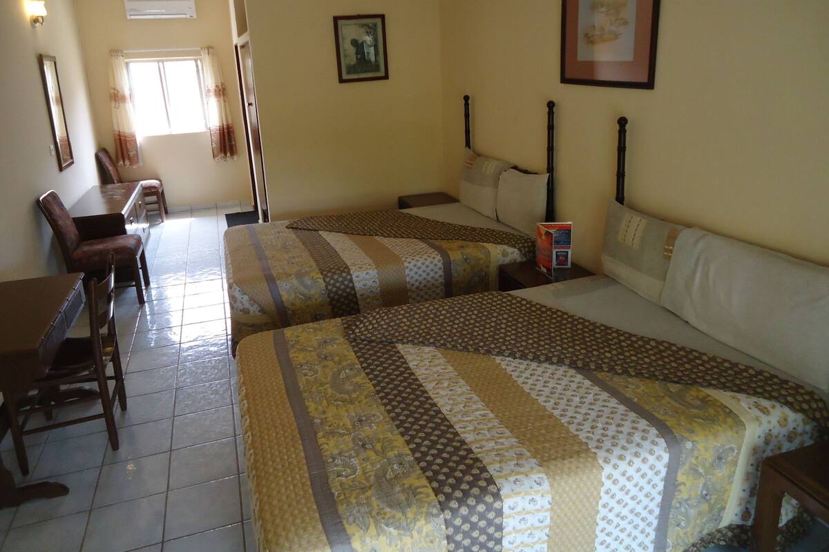 A hotel room with two beds, a desk, chairs, and a window.