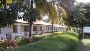 A row of white buildings with a covered walkway, surrounded by lush greenery and palm trees. - Holiday Beach Club Hotel (Serrekunda)