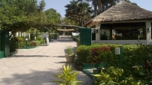 A pathway leading to a building with a thatched roof, surrounded by lush greenery and potted plants. - Holiday Beach Club Hotel (Serrekunda)