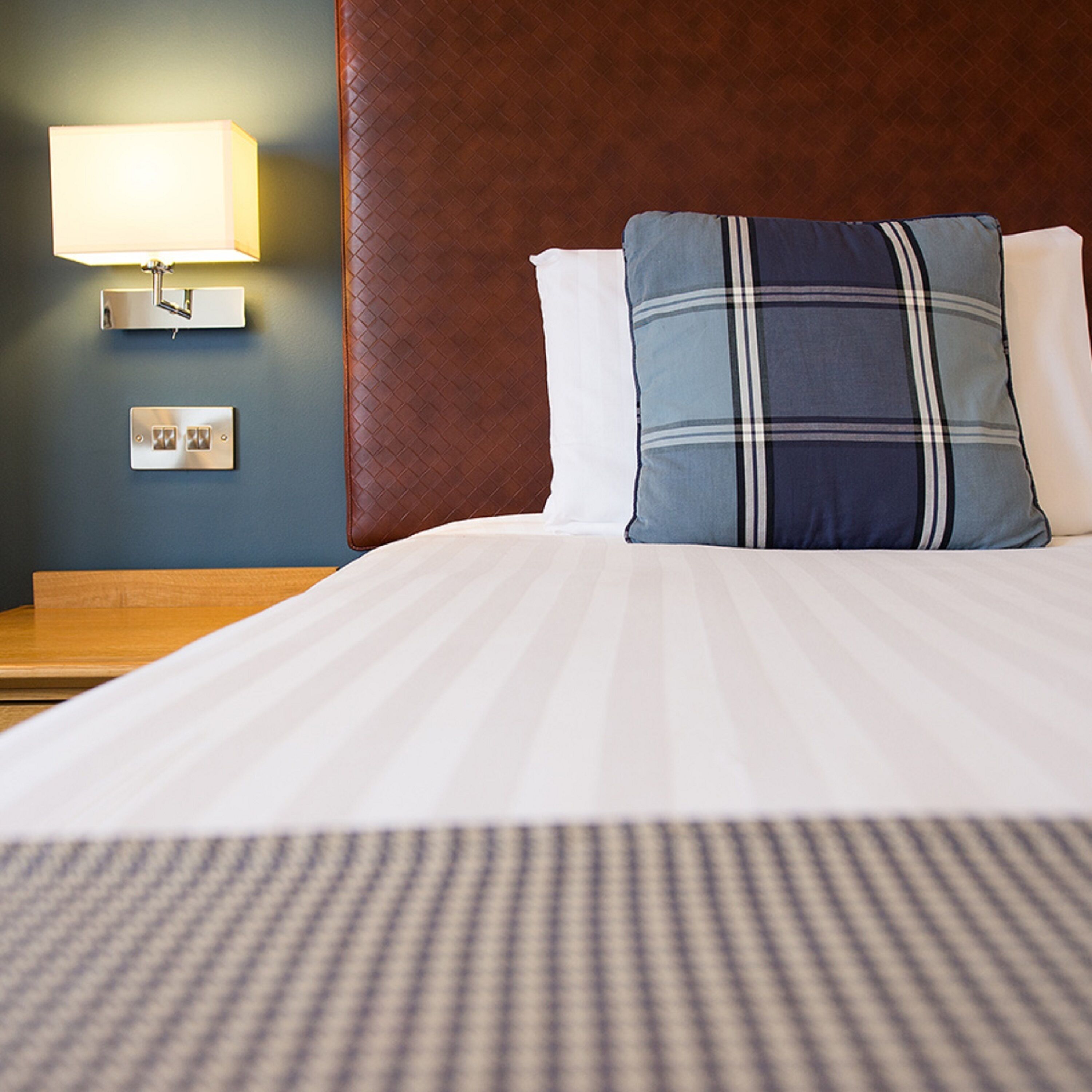 A neatly made bed with a striped bedspread, a blue and white pillow, and a wall-mounted lamp.