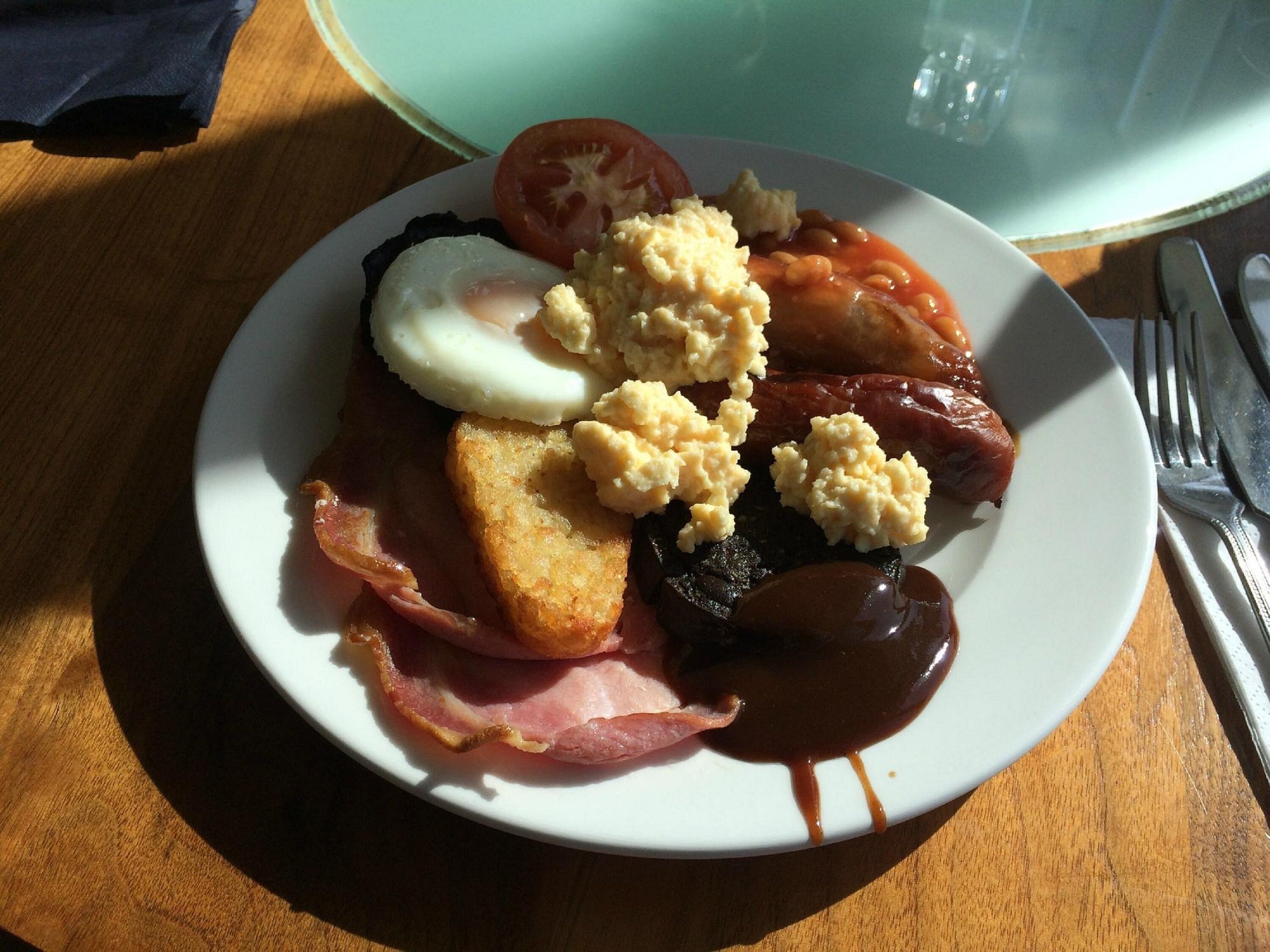 A plate of breakfast food including eggs, bacon, tomatoes, beans, and toast.