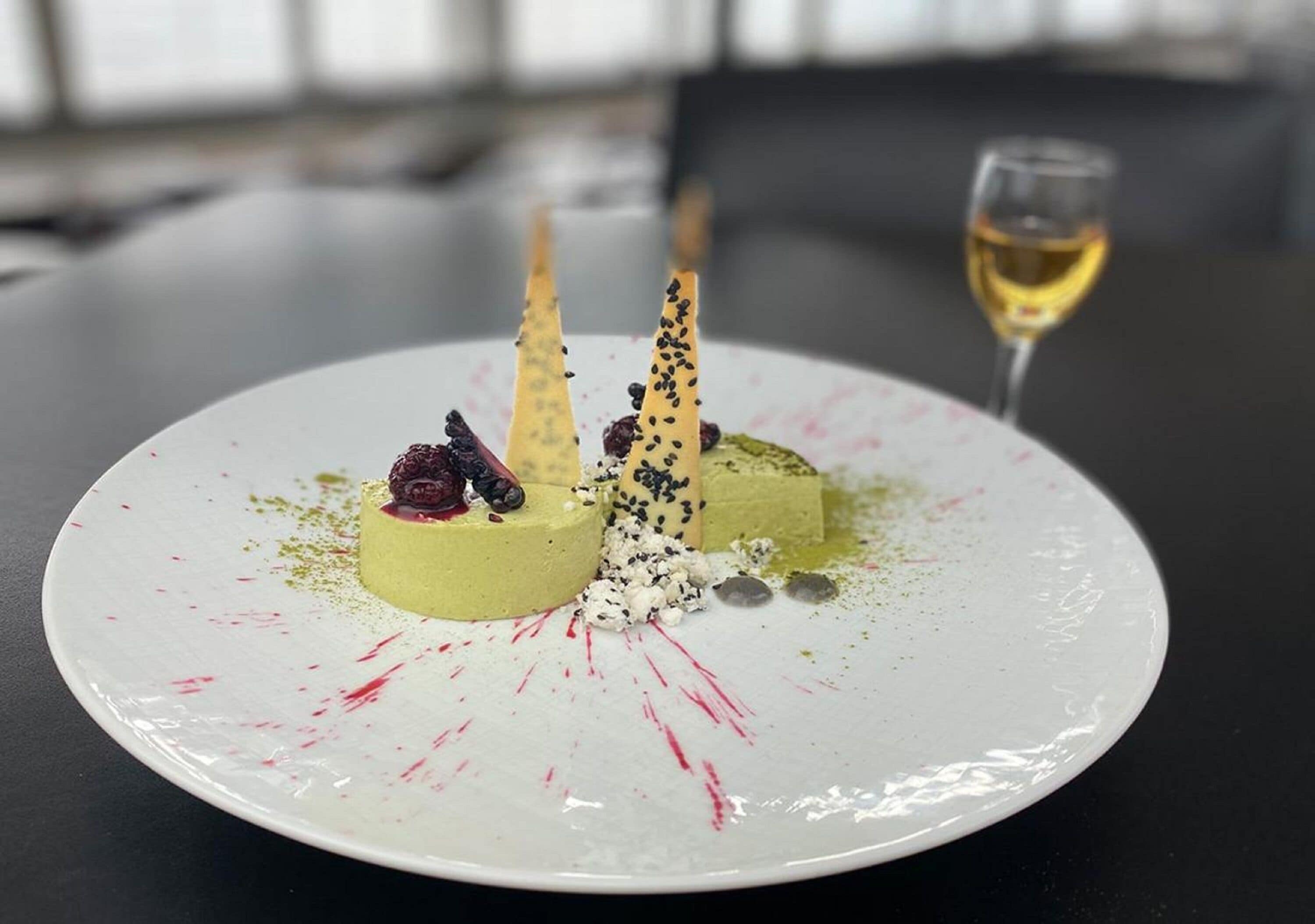 A dessert plate with three conical treats, a glass of white wine, and a white plate with red splatter.