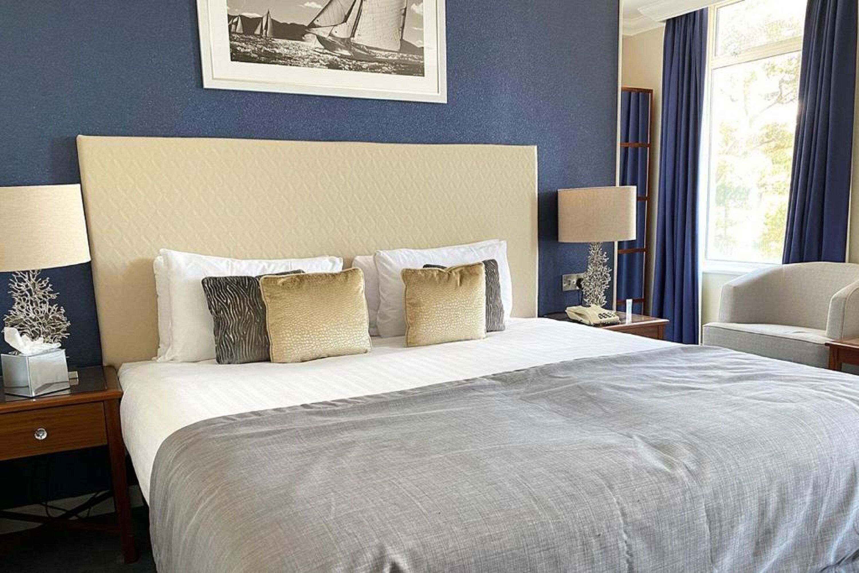 A hotel room with a large bed, two bedside tables, a nightstand, a chair, and a window with curtains.