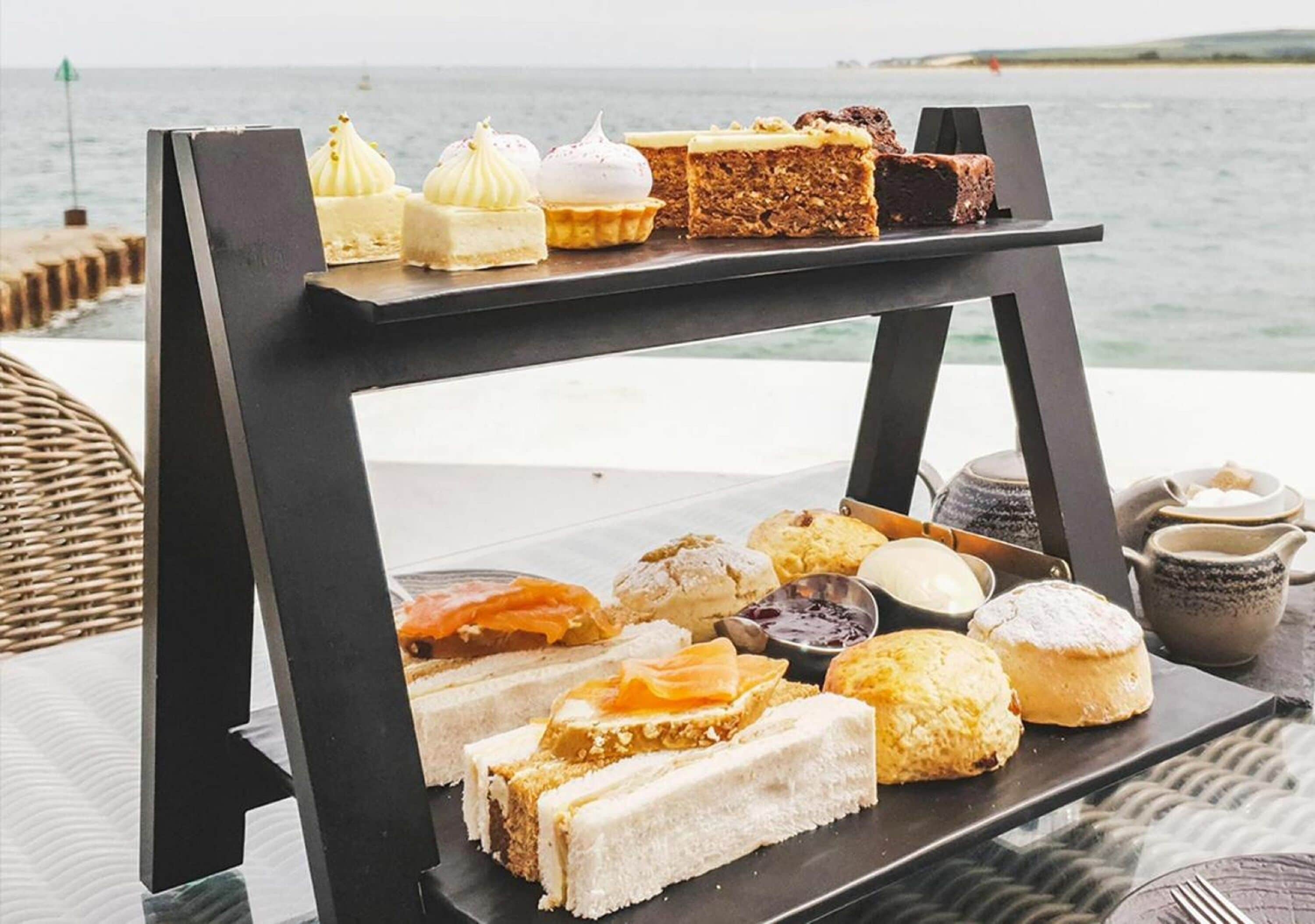 Un chariot de desserts, garni de diverses pâtisseries et de gâteaux, est placé sur une table au bord de la mer.