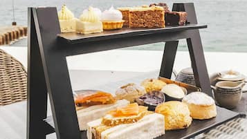 Un chariot de desserts, garni de diverses pâtisseries et de gâteaux, est placé sur une table au bord de la mer.