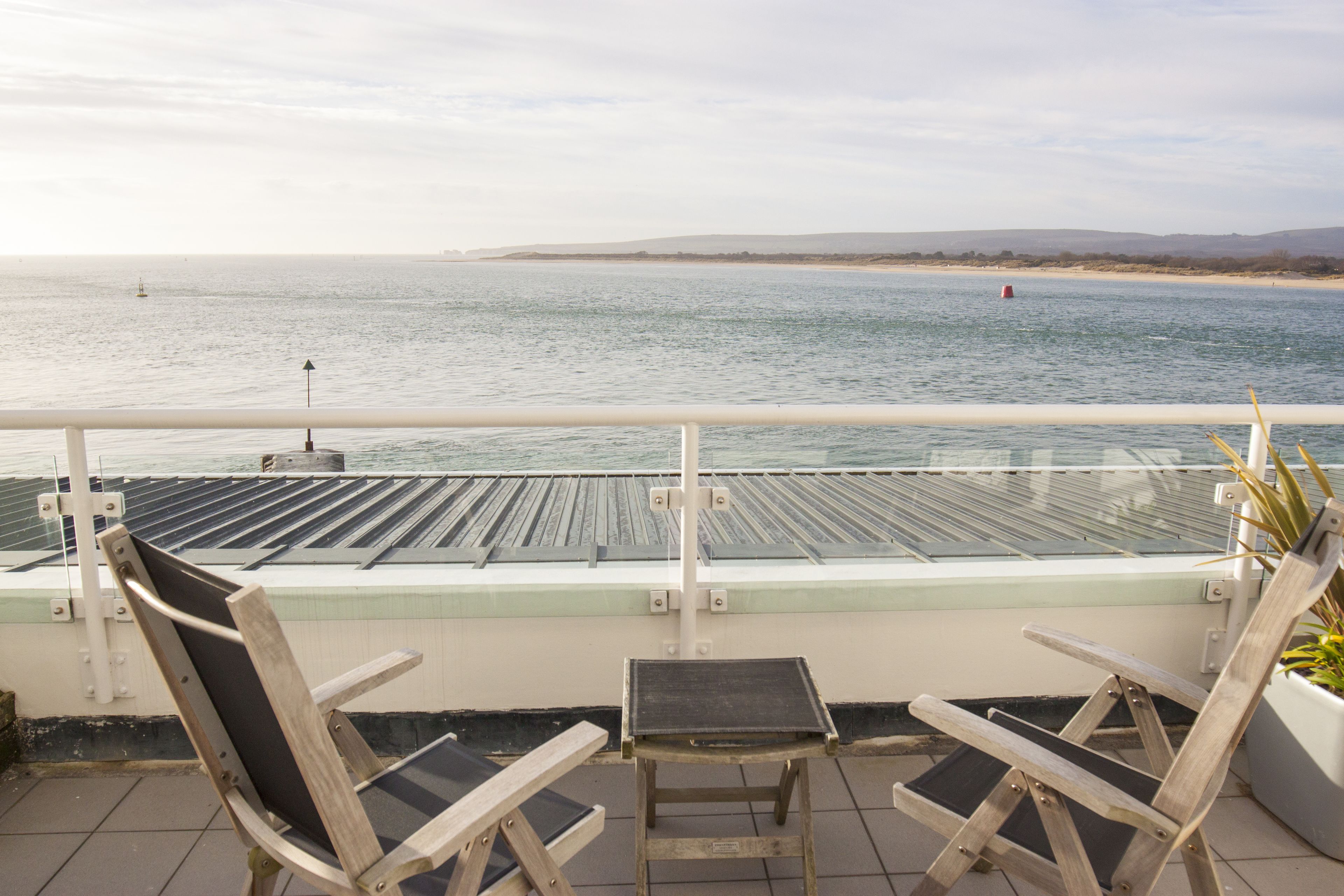A balcony with a view of the sea, two wooden chairs, and a small table.