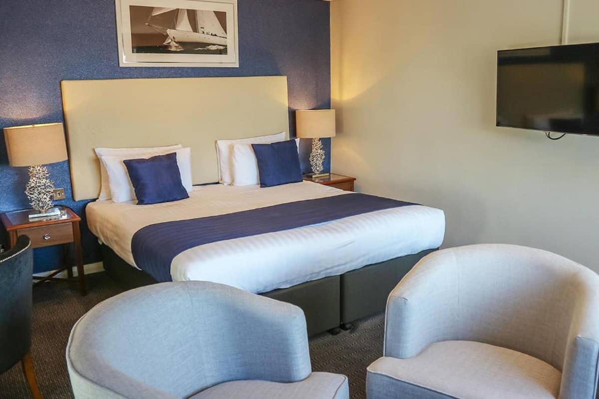 Una habitación de hotel con una cama grande, dos mesitas de noche con lámparas, un televisor de pantalla plana y dos sillones.