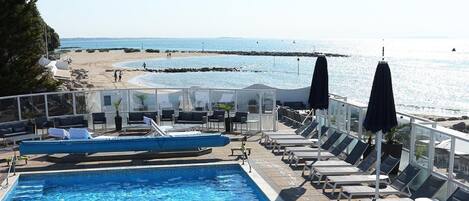 A pool area with lounge chairs and umbrellas, overlooking a beach and the sea.