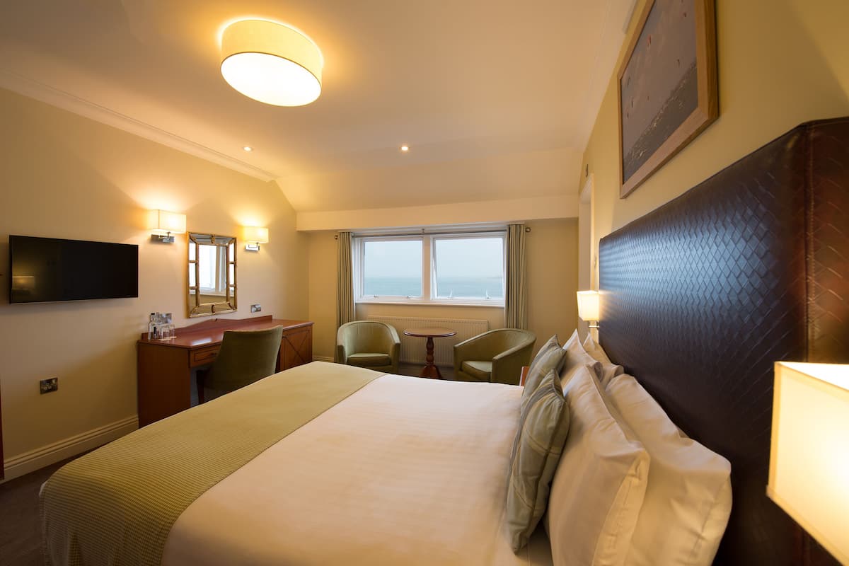 Habitación de hotel con una cama grande, un escritorio, dos sillas, un televisor y una ventana con vistas.