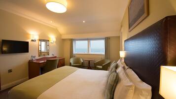 Une chambre d’hôtel avec un grand lit, un bureau, deux chaises, une télévision et une fenêtre donnant sur un beau paysage.