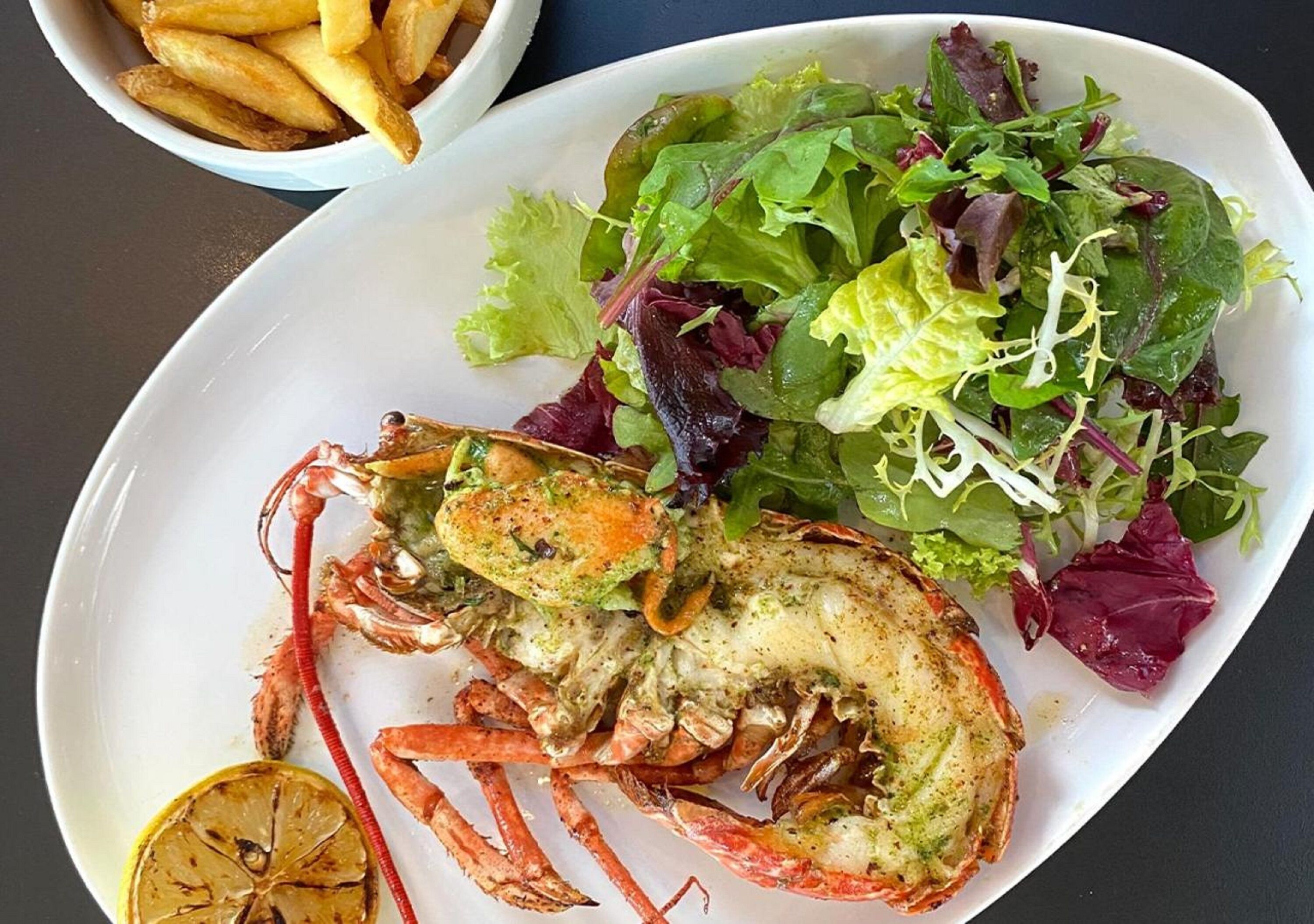 A plate with a cooked crab, a salad, and a bowl of fries.