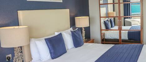 Habitación de hotel con una cama grande, dos lámparas de noche, una mesita de noche, un espejo y vistas al mar.