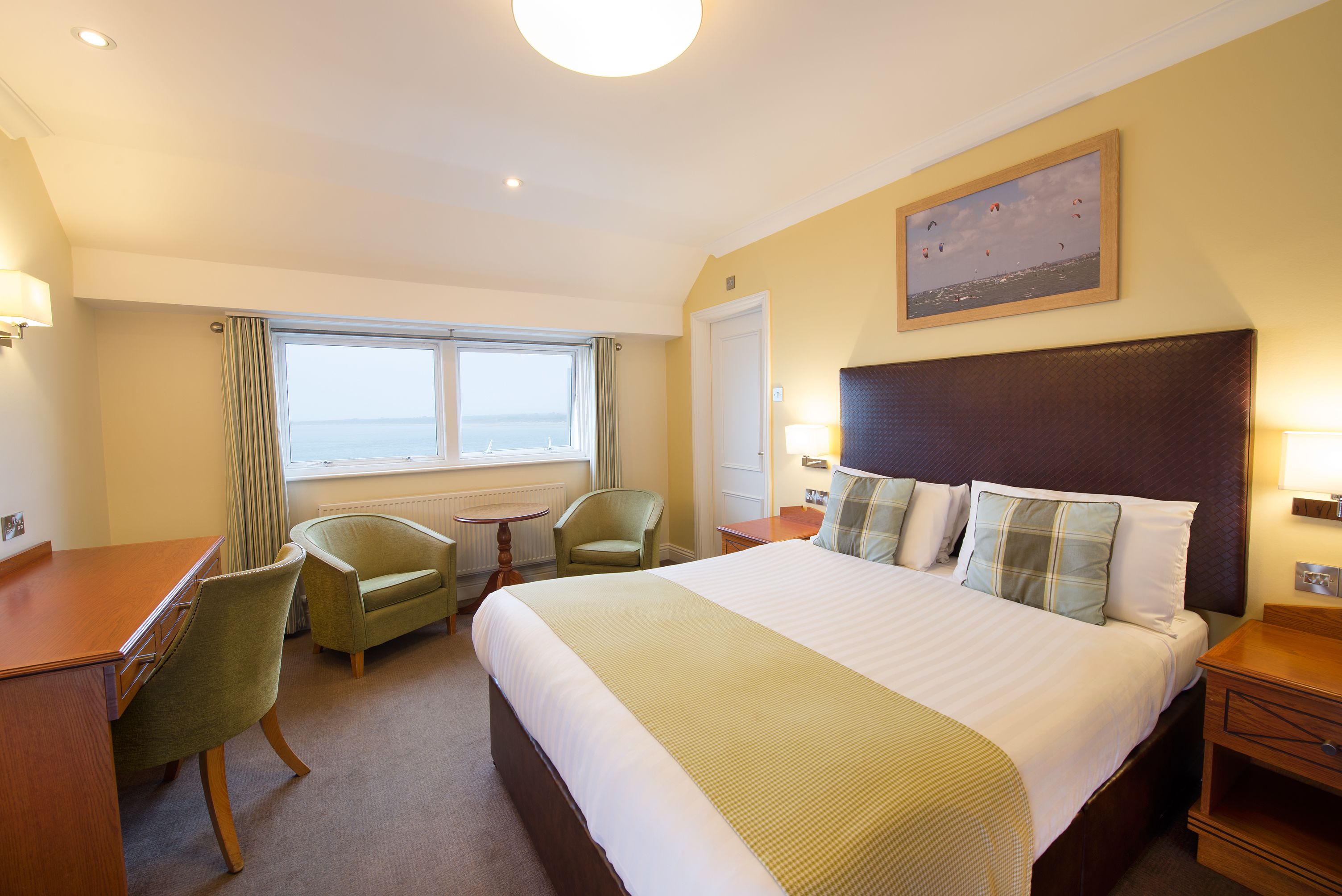 A hotel room with a large bed, a desk, two chairs, a small table, and a window with curtains.