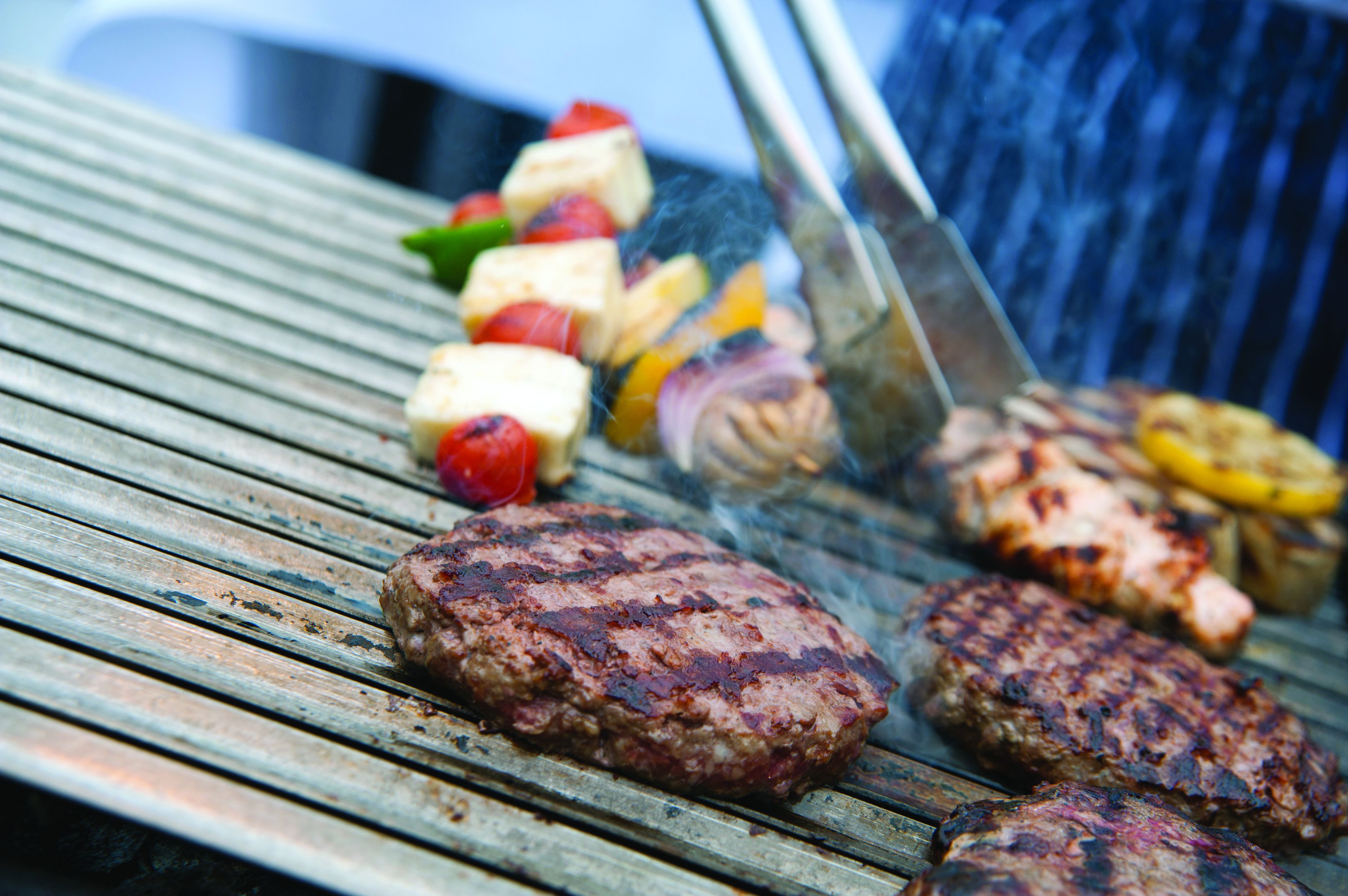 A grill with multiple burgers and vegetables being cooked.