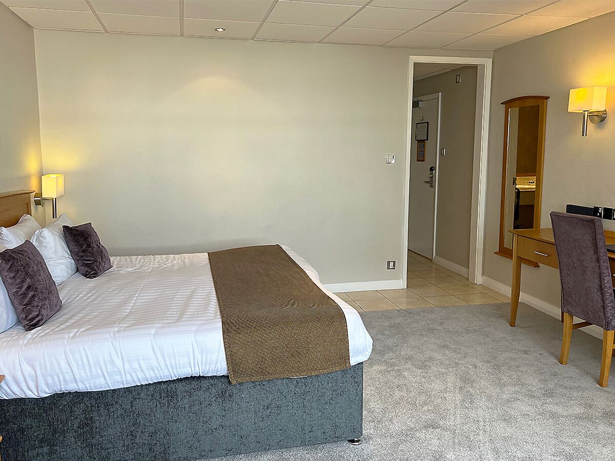 A hotel room with a bed, a desk, a chair, a lamp, and a mirror.