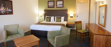 A hotel room with a bed, two armchairs, a wooden table, a desk, and a mirror.