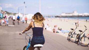 En person cykler på en asfalteret sti tæt på en strand, med cykler parkeret langs siden.