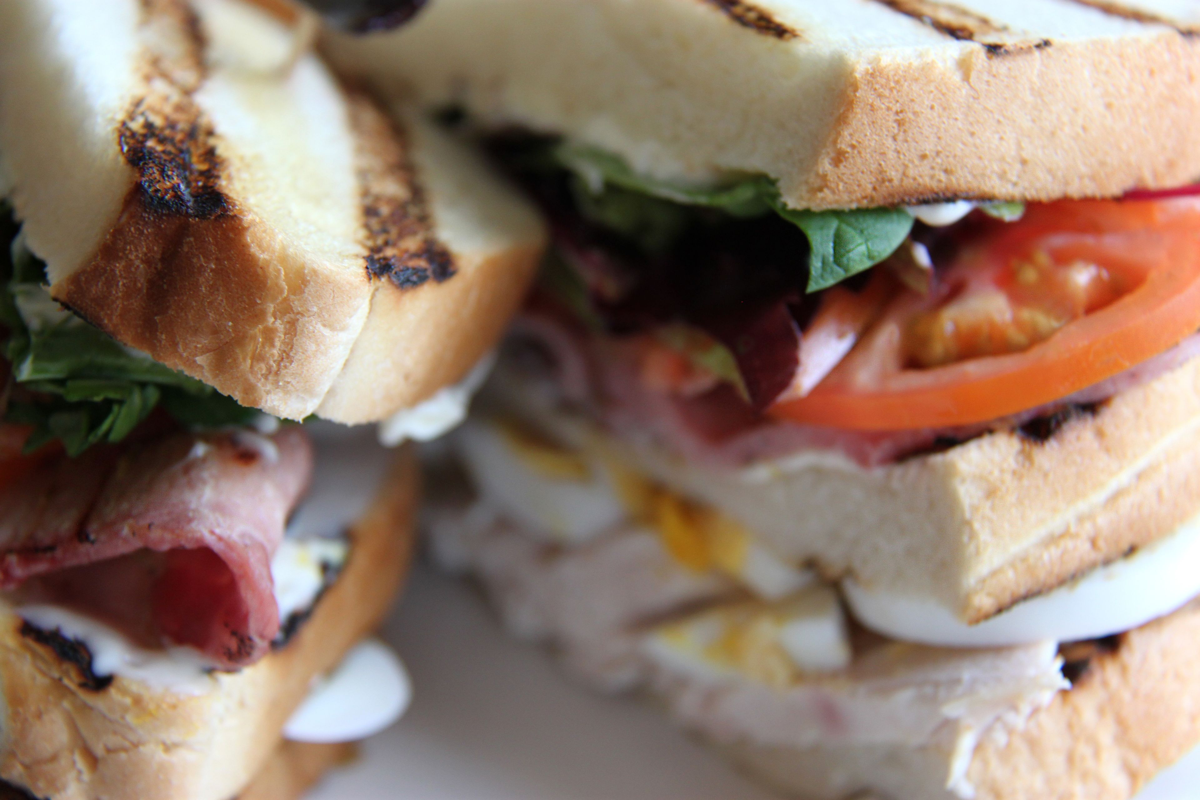 Un sándwich con ingredientes visibles como lechuga, tomate y, posiblemente, jamón, sobre pan tostado.