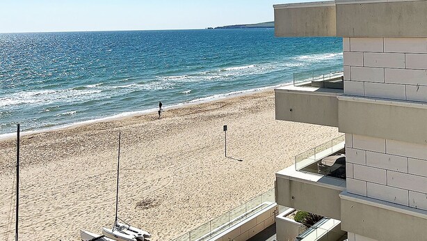 Una playa con una vista despejada del océano y un edificio con balcón que da a la playa.
