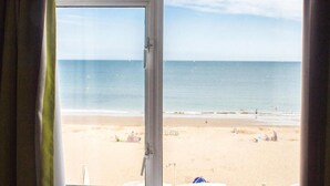 Vista de una playa desde una habitación con un ventanal grande, cortinas y vista al océano.