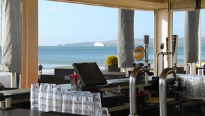 Zona de bar con vista al mar y un barco a lo lejos.