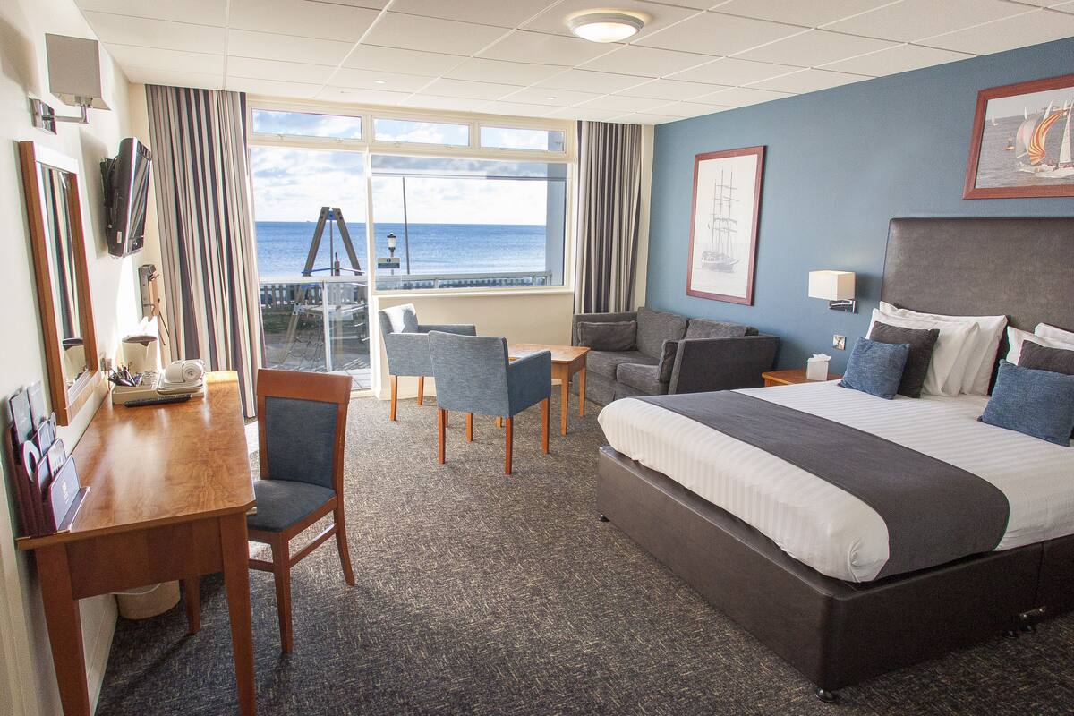 A hotel room with a large bed, a desk, a chair, and a view of the ocean.
