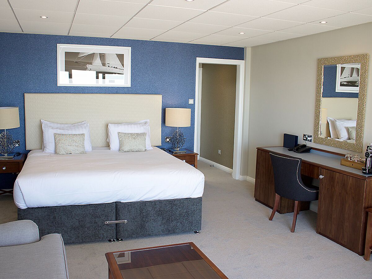 A hotel room with a large bed, a desk, a chair, a small table, and a mirror.