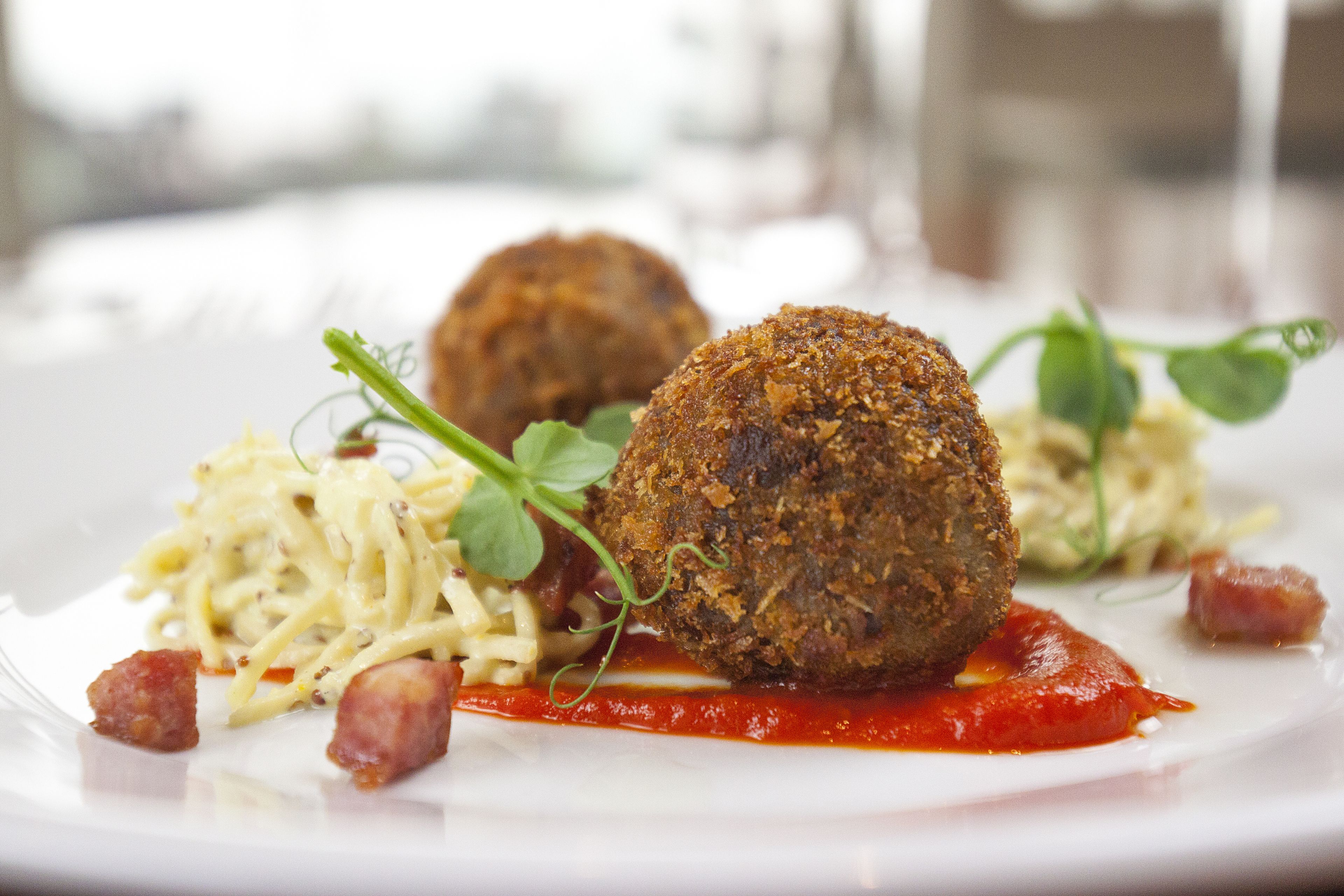 Un plato con dos albóndigas fritas, pasta y salsa.