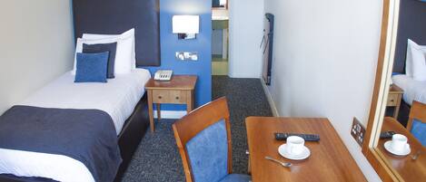 Une chambre d’hôtel avec deux lits, un bureau en bois, une chaise, un miroir et une petite table sur laquelle se trouvent une tasse et une télécommande.
