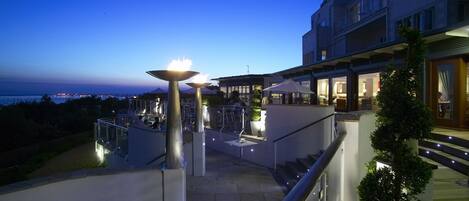 A modern hotel with outdoor seating, a pool, and a view of the sea.