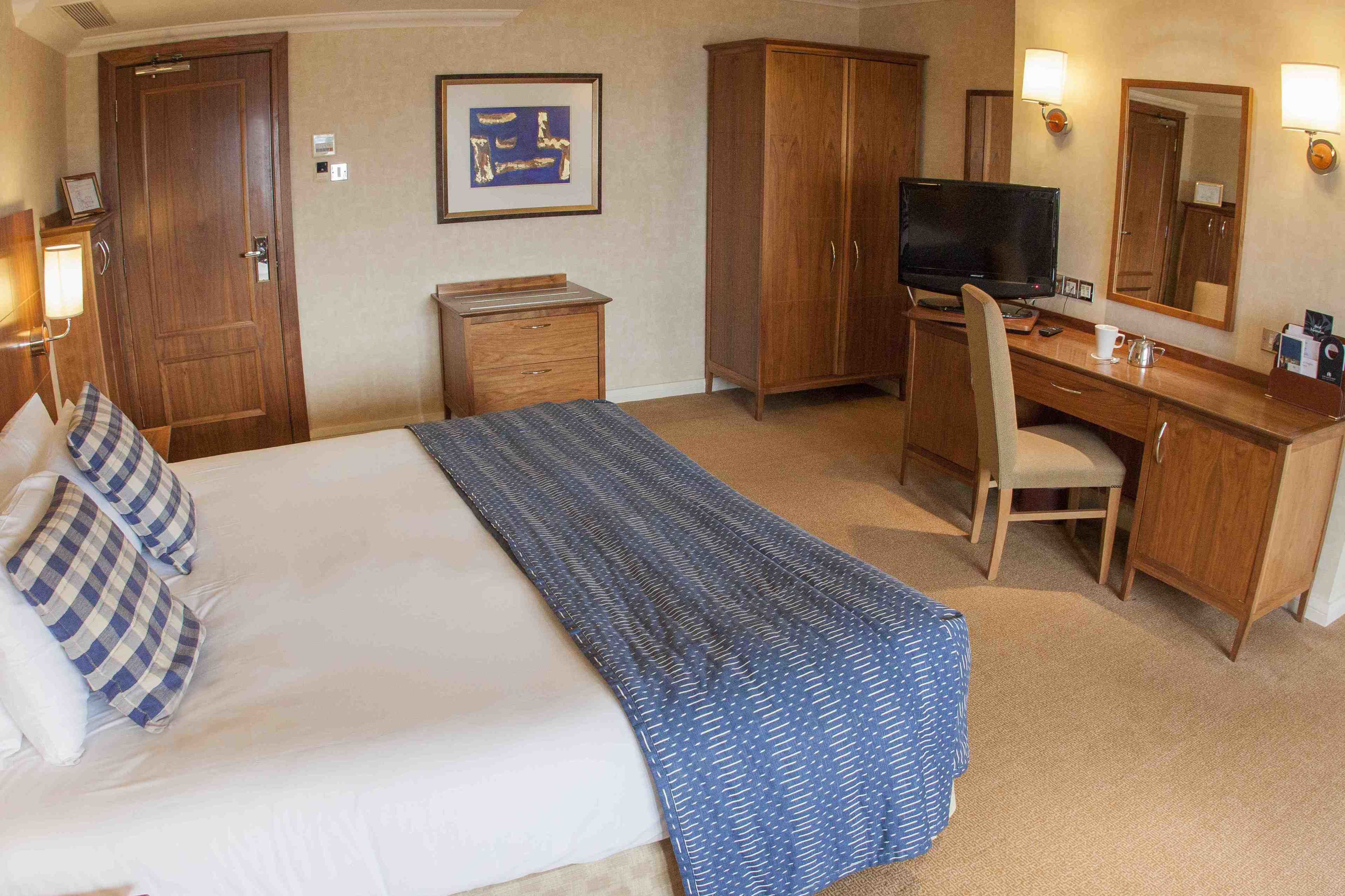 Una habitación de hotel con cama, escritorio, televisor, silla y armario.