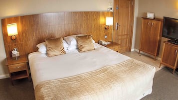 Ein Hotelzimmer mit einem großen Bett, einem Holzkopfstück, Nachttischlampen, einem Fernseher und einem Kleiderschrank.