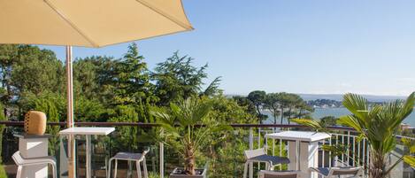 A balcony with outdoor furniture, a large umbrella, and a view of the sea.