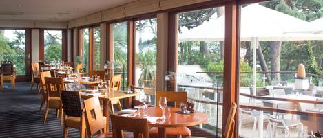 A restaurant with multiple tables and chairs, large windows offering a view of the outdoors.