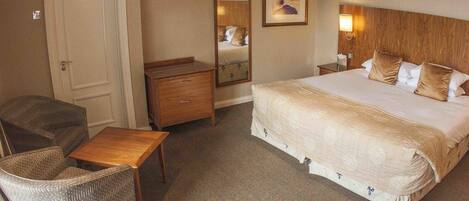 A hotel room with a bed, a wooden nightstand, a dresser, a chair, and a small table.